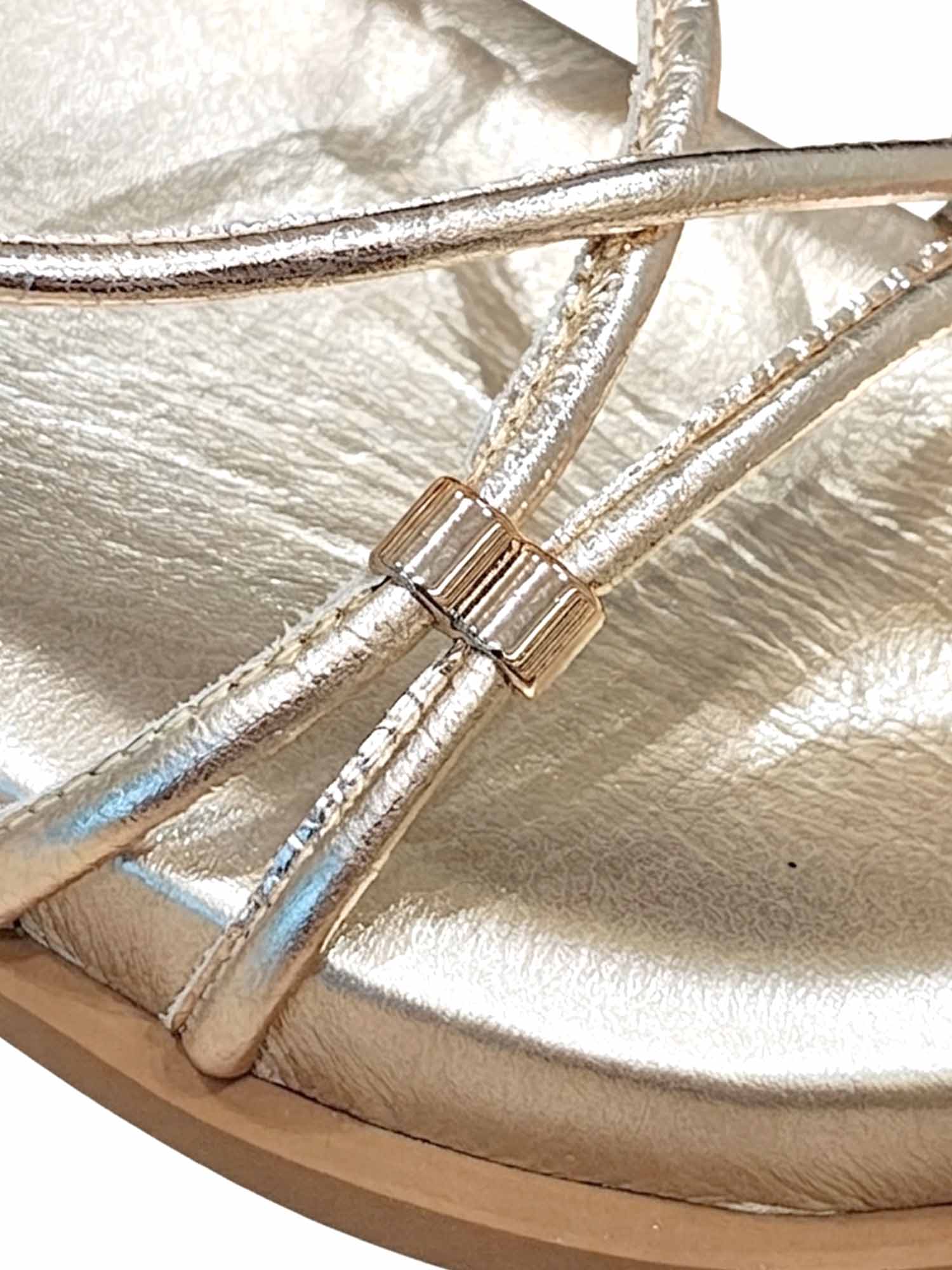 Primer plano del brillo metálico en las tiras doradas y el detalle metálico de ajuste en la sandalia Begonia