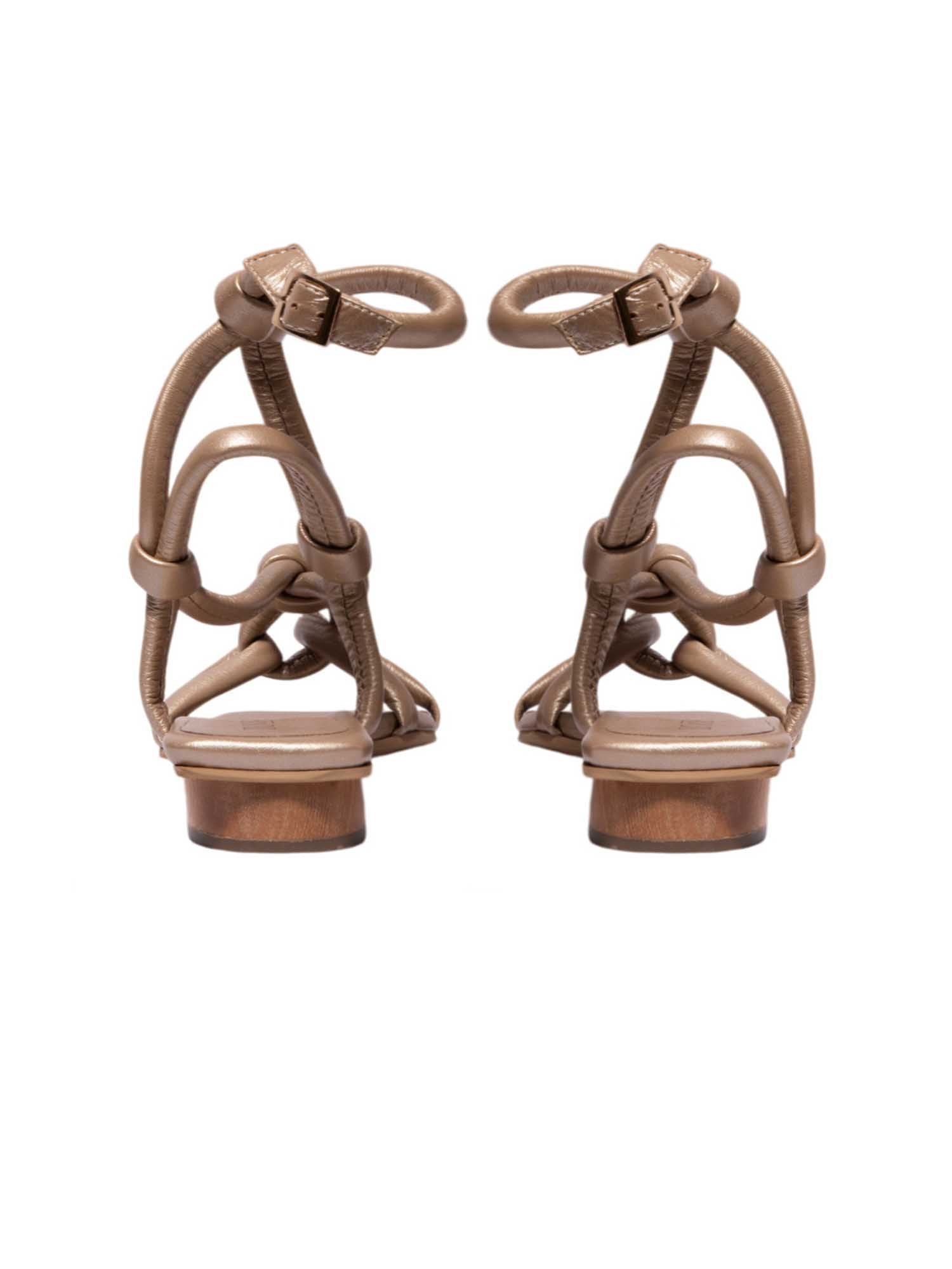 Vista posterior de la sandalia Duna dorada, destacando cómo las tiras metalizadas envuelven el pie y contrastan con su mini tacón en madera