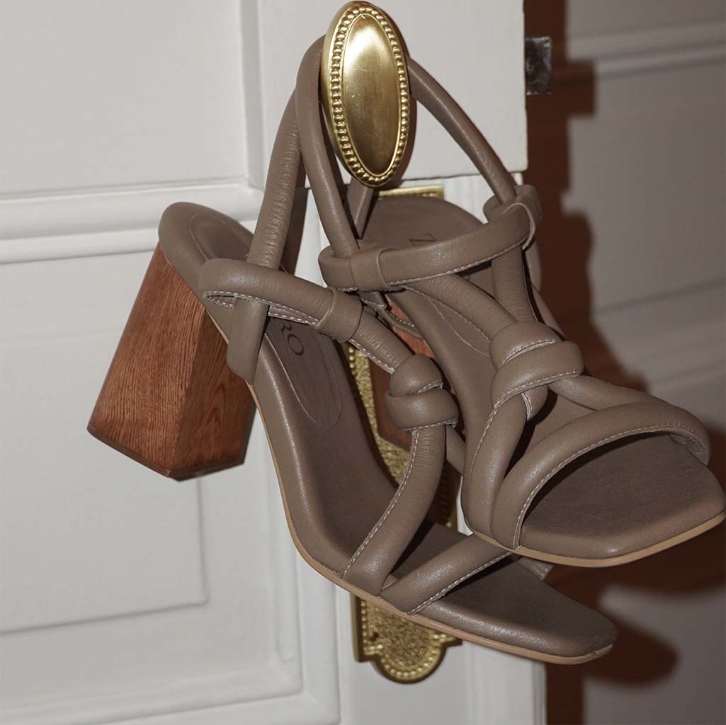 Tacón modelo Prata color beige colgado en el pomo dorado de una elegante puerta blanca