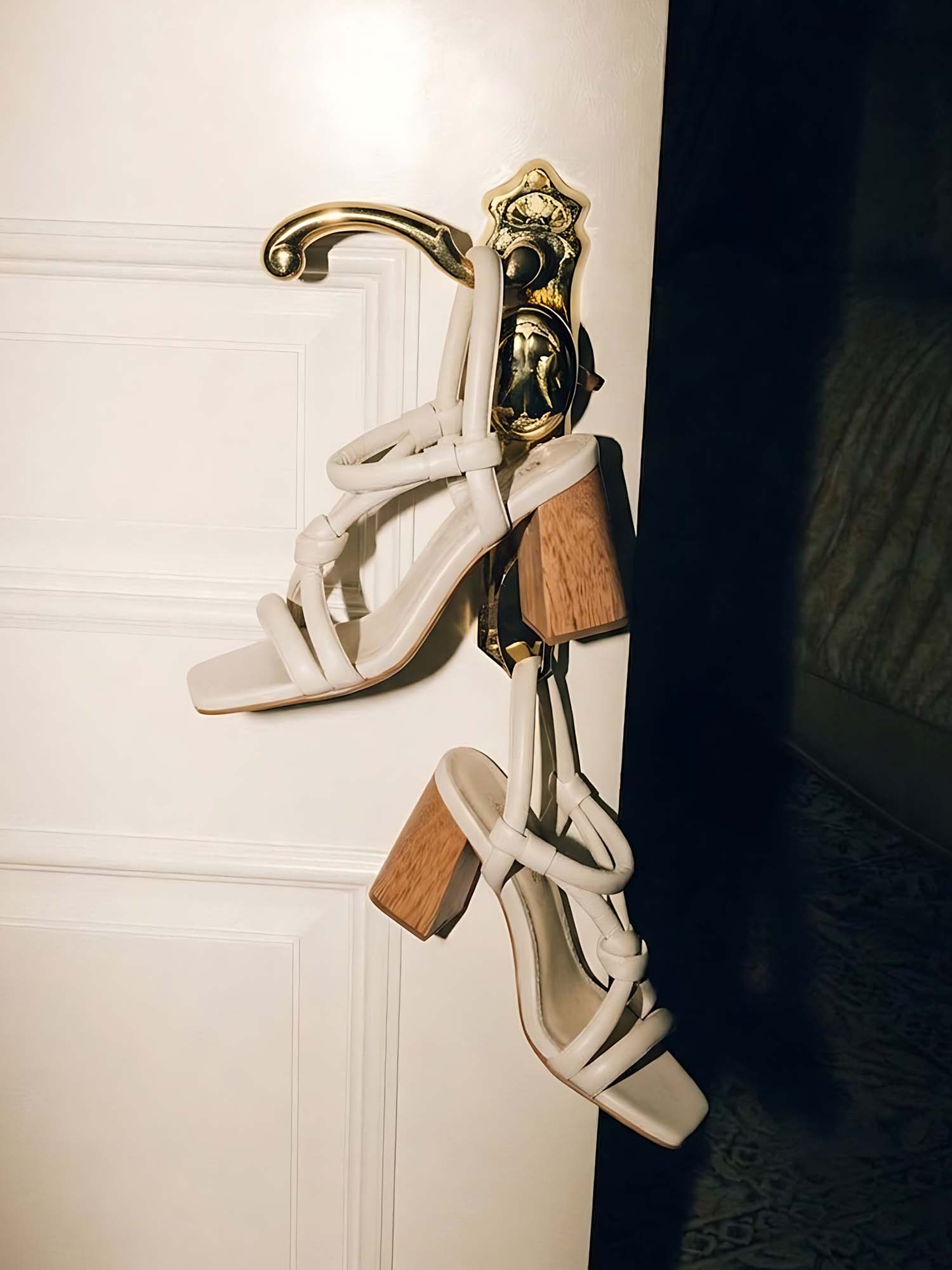 Tacón modelo Prata color talco colgado en la manija dorada de una elegante puerta blanca