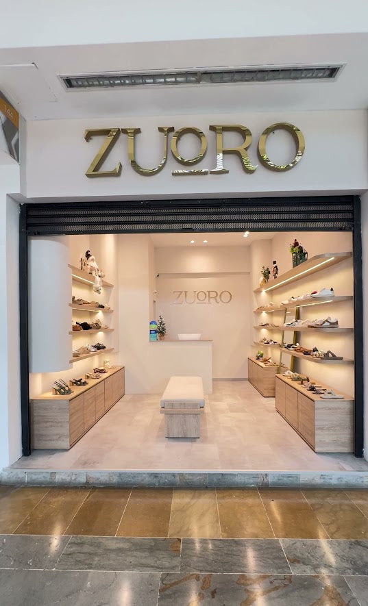 Vista exterior de tienda de sandalias Zuoro Shoes en el centro comercial Unicentro, con estantes de calzado a los lados y una silla central para medirse los productos